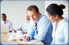 Male businessman reviewing notes at conference table with female colleague.